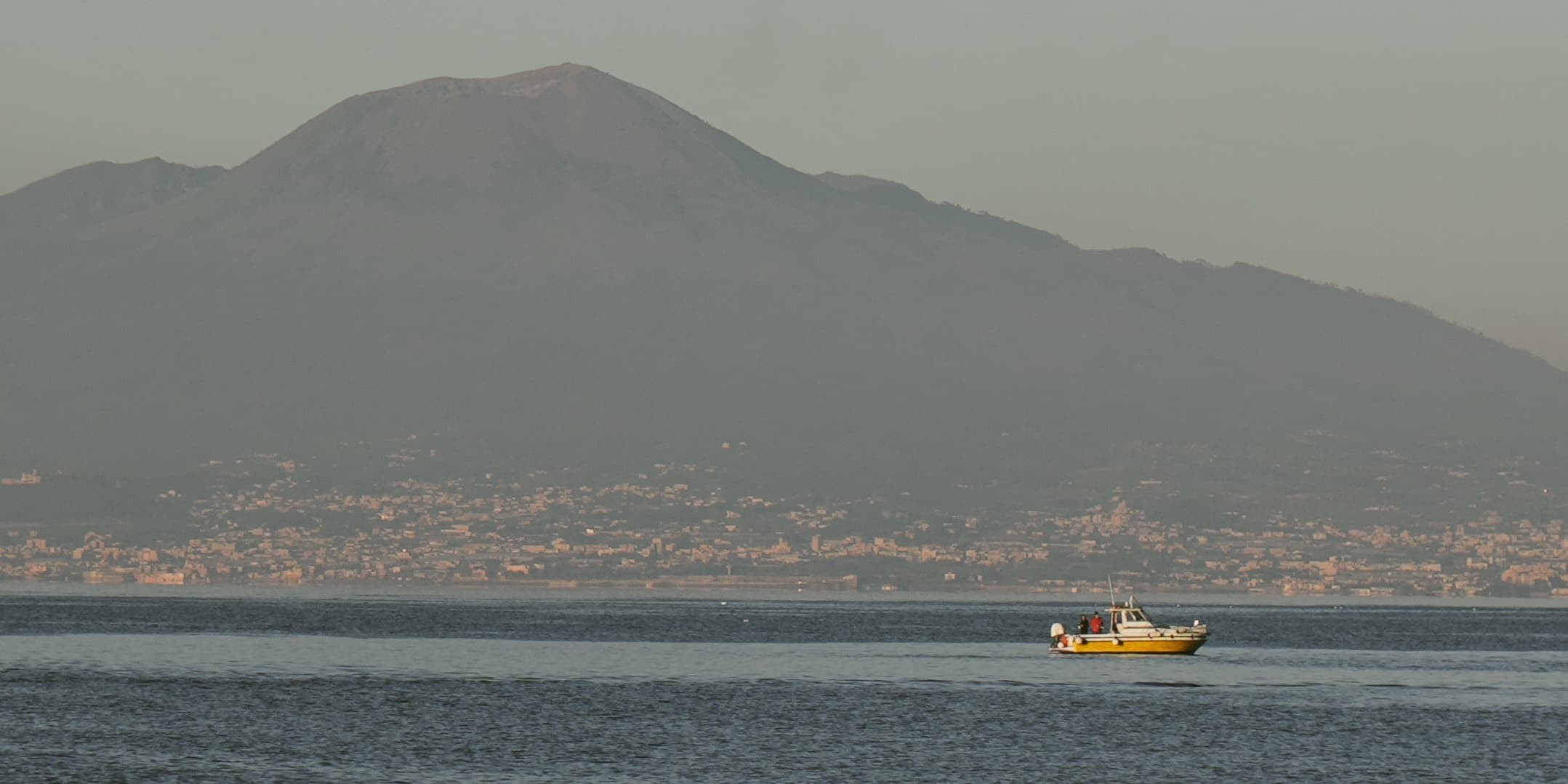 Yellow passenger boat crossing a bay beneath a volcanic mountain photographed by Eugene Truuts