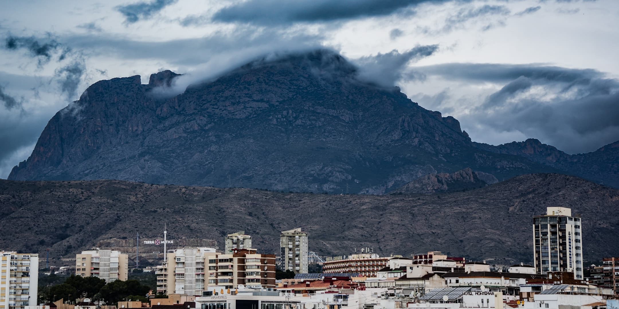 Coastal city beneath a cloud-covered mountain photographed by Eugene Truuts